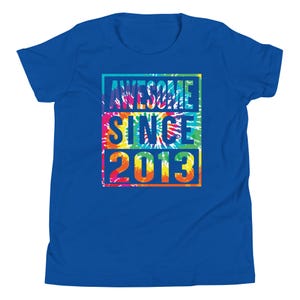 May include: A royal blue t-shirt featuring the text "AWESOME SINCE 2013" in a tie-dye design. The text is stacked in a rectangular shape. The shirt is made of a soft material and is suitable for casual wear.