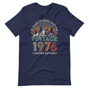 May include: Navy blue t-shirt with a vintage design. The graphic includes the text "50 YEARS OF BEING AWESOME" in a circular design, with "VINTAGE 1976 LIMITED EDITION" below a mountain scene.