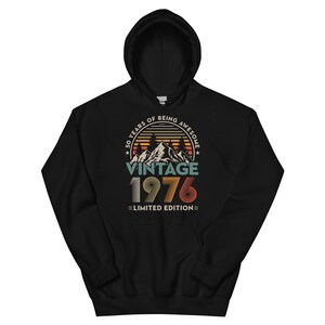 May include: Black hooded sweatshirt with a vintage design. The design includes the text "50 YEARS OF BEING AWESOME" and "VINTAGE 1976 LIMITED EDITION" with a mountain and sunset graphic. The hoodie has a front pocket.