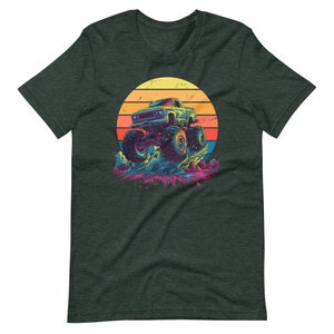 May include: Dark grey t-shirt with a vibrant graphic of a monster truck leaping. The design incorporates a retro sunset in yellow, orange, and red hues. The truck is blue and green, with oversized tyres, set against a splash of colourful water.