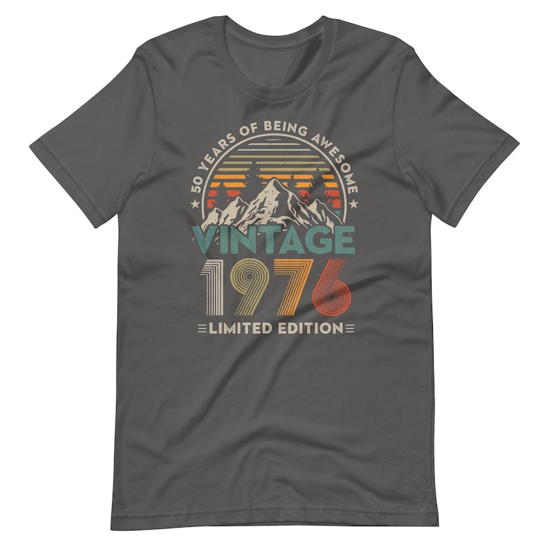 May include: Dark gray t-shirt with a vintage design. The graphic includes the text "50 YEARS OF BEING AWESOME" in a circular pattern, with "VINTAGE 1976 LIMITED EDITION" below a mountain and sunset illustration.