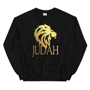 Op de afbeelding: Zwarte sweatshirt met een gouden leeuwenkopafbeelding en het woord "JUDAH" in gouden letters. De crewneck-sweatshirt heeft een geribbelde kraag, manchetten en zoom. De leeuwenafbeelding is gedetailleerd en gestileerd.
