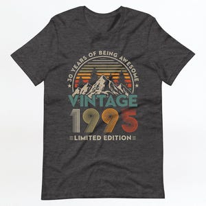May include: Dark grey t-shirt with a vintage-style graphic design. The graphic features a mountain range with a sunset behind it and the text "30 Years of Being Awesome Vintage 1995 Limited Edition".