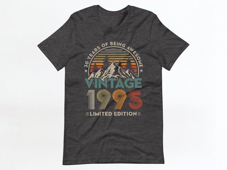 May include: Dark grey t-shirt with a vintage-style graphic design. The graphic features a mountain range with a sunset behind it and the text "30 Years of Being Awesome Vintage 1995 Limited Edition".