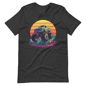 May include: Dark grey t-shirt with a vibrant graphic of a monster truck leaping over water. The design includes a sunset with yellow, orange, and red stripes. The truck is blue and green, set against a colourful backdrop.