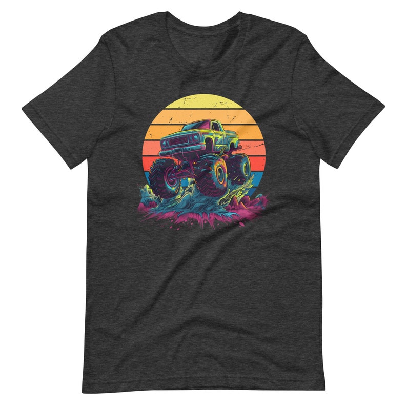 May include: Dark grey t-shirt with a vibrant graphic of a monster truck leaping over water. The design includes a sunset with yellow, orange, and red stripes. The truck is blue and green, set against a colourful backdrop.