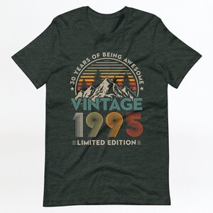 May include: A dark green t-shirt with a vintage-style graphic that says "30 Years of Being Awesome Vintage 1995 Limited Edition". The graphic features a mountain range with a sunset behind it.