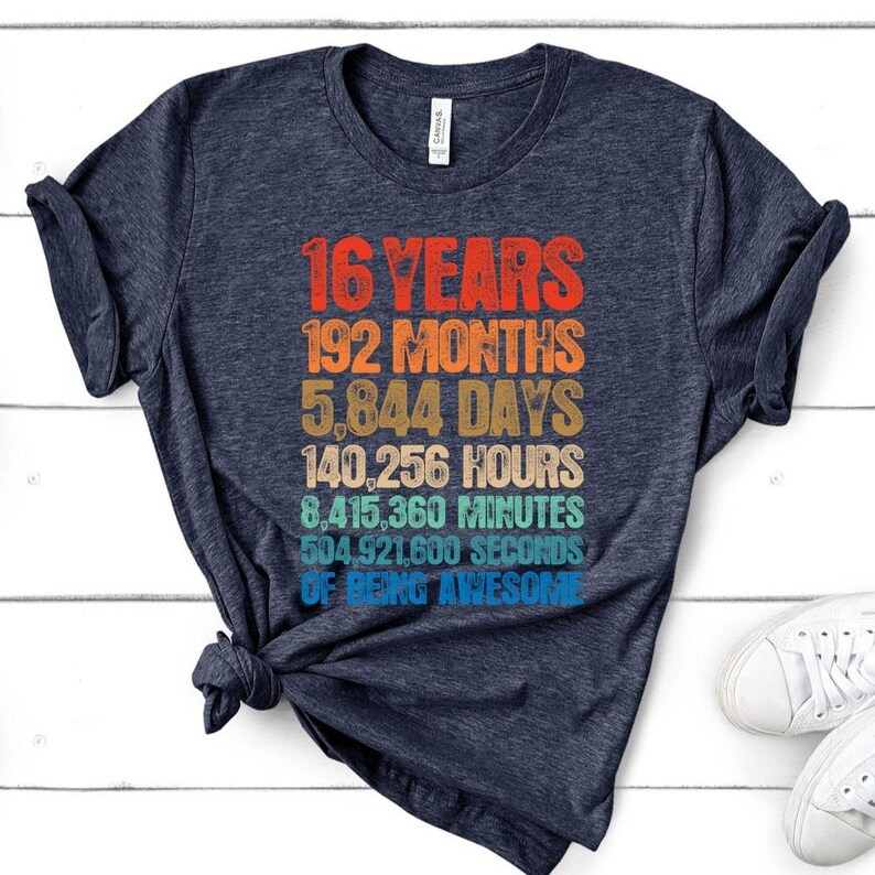 May include: A dark heather navy blue t-shirt featuring a multi-colored retro-style graphic with the text: 16 YEARS, 192 MONTHS, 5,844 DAYS, 140,256 HOURS, 8,415,360 MINUTES, 504,921,600 SECONDS OF BEING AWESOME in stacked, distressed lettering.