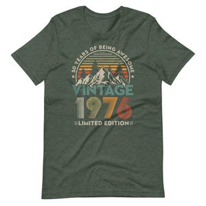 May include: A dark green t-shirt with a vintage design. The design includes the text "50 YEARS OF BEING AWESOME" in a circular frame, with "VINTAGE 1976 LIMITED EDITION" below a mountain graphic.