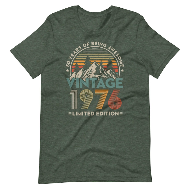 May include: A dark green t-shirt with a vintage design. The design includes the text "50 YEARS OF BEING AWESOME" in a circular frame, with "VINTAGE 1976 LIMITED EDITION" below a mountain graphic.