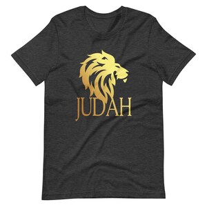 Op de afbeelding: Donkergrijs t-shirt met een gouden leeuwenkop ontwerp en het woord "JUDAH" in gouden letters. De manen van de leeuw zijn gedetailleerd en de tekst is gecentreerd onder de leeuw. Een casual T-shirt met korte mouwen.