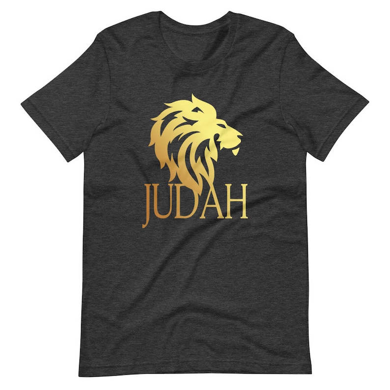 Op de afbeelding: Donkergrijs t-shirt met een gouden leeuwenkop ontwerp en het woord "JUDAH" in gouden letters. De manen van de leeuw zijn gedetailleerd en de tekst is gecentreerd onder de leeuw. Een casual T-shirt met korte mouwen.