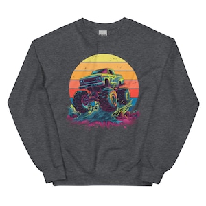 May include: Dark grey sweatshirt with a graphic of a monster truck. The truck is set against a sunset with orange, yellow, and red colours. The monster truck has large tyres and is in motion.