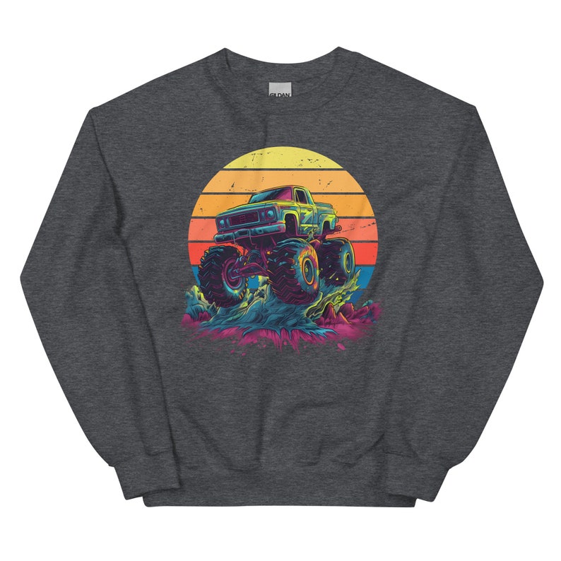 May include: Dark grey sweatshirt with a graphic of a monster truck. The truck is set against a sunset with orange, yellow, and red colours. The monster truck has large tyres and is in motion.