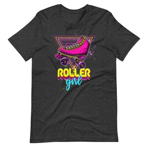 May include: Dark grey t-shirt with a graphic of a pink roller skate with purple wheels, set against a neon triangle. The words "ROLLER girl" are in a retro font, with a splash of blue and yellow.