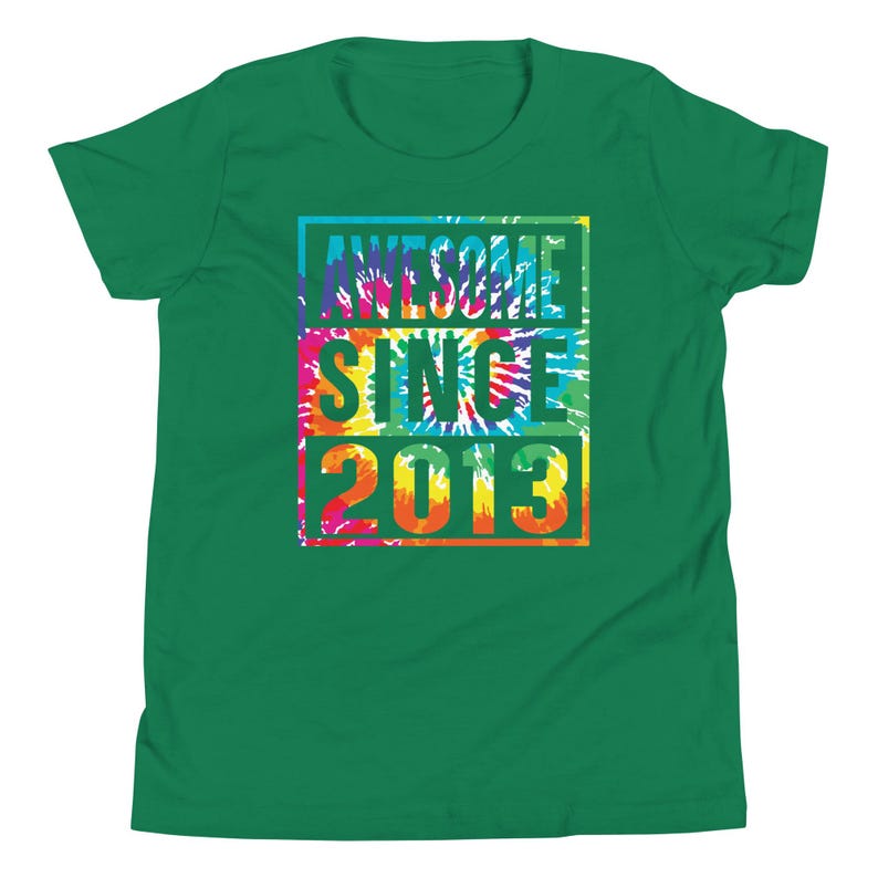 May include: A green t-shirt featuring the text "AWESOME SINCE 2013" in a tie-dye design. The text is in a rectangular shape with blue, pink, yellow, and orange colours. The shirt is a solid green colour.