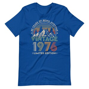 May include: Royal blue t-shirt with a vintage design. The graphic features a mountain scene with the text "50 YEARS OF BEING AWESOME" in a circle, "VINTAGE 1976" below, and "LIMITED EDITION" at the bottom. The design uses orange, green, and white.