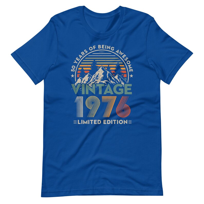 May include: Royal blue t-shirt with a vintage design. The graphic features a mountain scene with the text "50 YEARS OF BEING AWESOME" in a circle, "VINTAGE 1976" below, and "LIMITED EDITION" at the bottom. The design uses orange, green, and white.