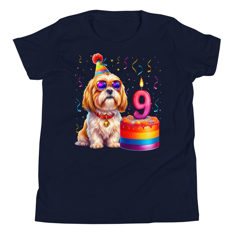 May include: Navy blue t-shirt featuring a cartoon dog wearing sunglasses and a party hat. The dog is next to a rainbow-colored cake with a lit candle shaped like the number 9. Colorful confetti is scattered around the design.