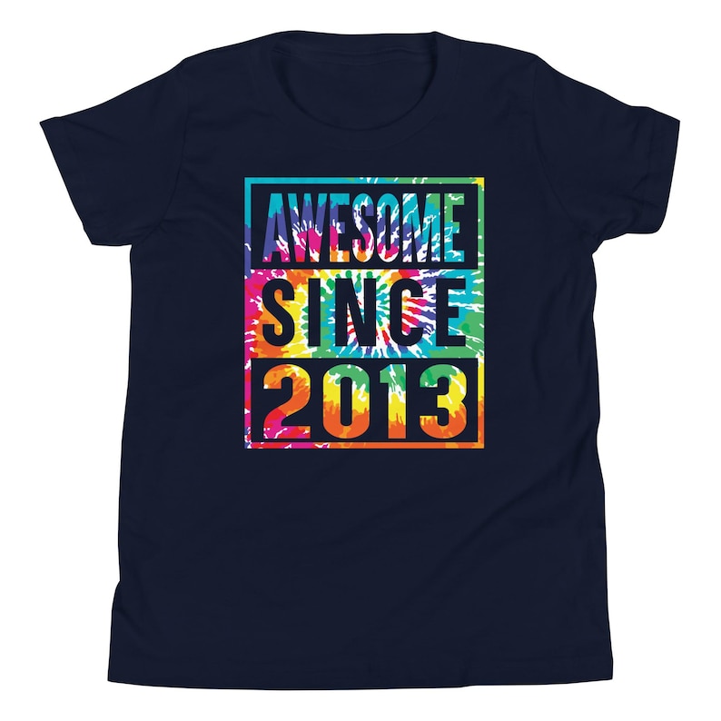 May include: Navy blue t-shirt with a colourful tie-dye design. The shirt features the text "AWESOME SINCE 2013" in a rectangular frame. The text is in white, yellow, orange, and blue. The shirt is a youth size.