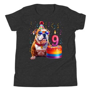 May include: Dark gray t-shirt featuring a colorful illustration of a bulldog wearing sunglasses and a party hat. The bulldog is next to a birthday cake with a number 9 candle, with confetti and streamers in the background.