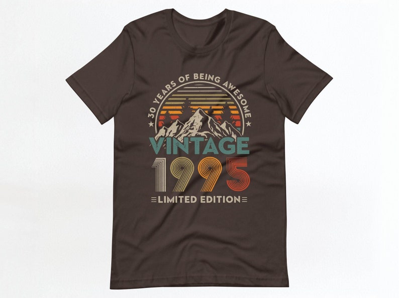 May include: A brown t-shirt with a vintage-style graphic that says "30 Years of Being Awesome Vintage 1995 Limited Edition". The graphic features a mountain range with a sunset behind it.