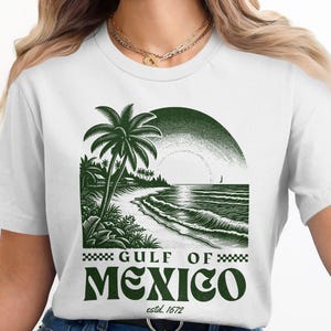 May include: White t-shirt with a green graphic design of a palm tree on a beach with the text "GULF OF MEXICO estd. 1672"