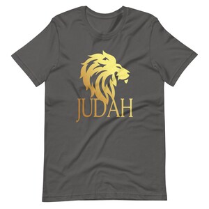 Op de afbeelding: Donkergrijs t-shirt met een gouden leeuw afbeelding en het woord "JUDAH". Het leeuwenontwerp is gedetailleerd en gestileerd, met een vloeiende manen. De tekst is vetgedrukt en zonder schreef.