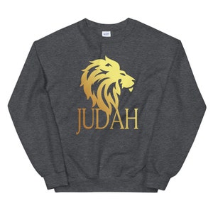 Op de afbeelding: Donkergrijze sweatshirt met een gouden leeuwenafbeelding en het woord "JUDAH" in goud. De leeuwenafbeelding is een gestileerd ontwerp met een manen en een profiel. De sweatshirt heeft een ronde hals.