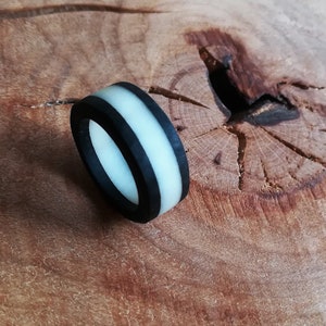 Könnte beinhalten: Ein schwarzer Silikonring mit einem weißen Streifen. Der Ring liegt auf einer Holzoberfläche.