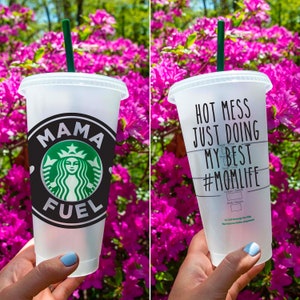 May include: Two clear plastic reusable cups with black text and graphics. The first cup says "Mama Fuel" with a green Starbucks logo. The second cup says "Hot Mess Just Doing My Best #MomLife".