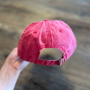 Puede incluir: Una gorra de b&eacute;isbol de algod&oacute;n roja con un aspecto desgastado. La gorra tiene un cierre de hebilla en la parte posterior.