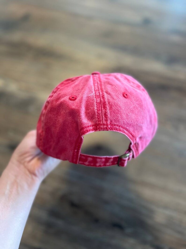 Puede incluir: Una gorra de b&eacute;isbol de algod&oacute;n roja con un aspecto desgastado. La gorra tiene un cierre de hebilla en la parte posterior.