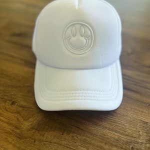 K&ouml;nnte beinhalten: Wei&szlig;e Trucker-Cap mit einem Smiley-Aufn&auml;her. Die Kappe hat einen gebogenen Schirm und eine Mesh-R&uuml;ckseite. Das Smiley-Gesicht ist auf der Vorderseite aufgestickt. Die Kappe besteht aus einem weichen, atmungsaktiven Material.