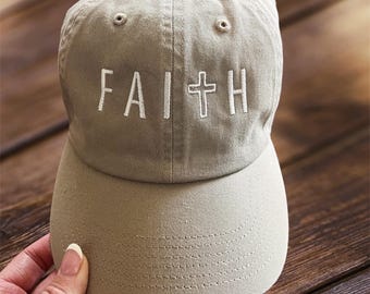 May include: A khaki baseball cap with a white embroidered cross and the word "FAITH" on the front.