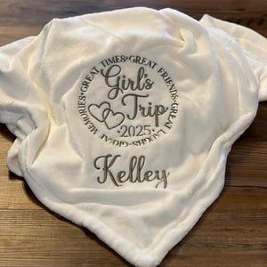 May include: White fleece blanket with embroidered text "Great Times, Great Friends, Great Memories, Great Laughs, Girl's Trip 2025" and the name "Kelley"