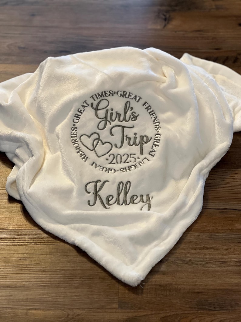 May include: White fleece blanket with embroidered text "Great Times, Great Friends, Great Memories, Great Laughs, Girl's Trip 2025" and the name "Kelley"