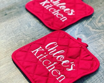 May include: Two red quilted pot holders with white embroidery that reads "Chloe's Kitchen".
