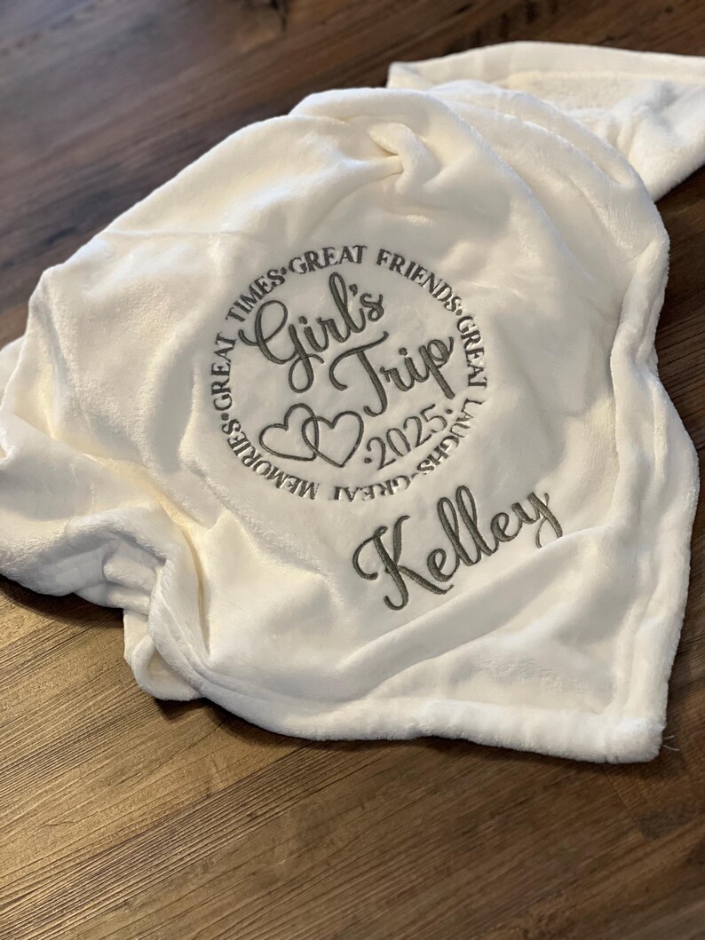 May include: White plush blanket with embroidered text "Girls Trip 2025" in a circle with hearts and the name "Kelley" below.