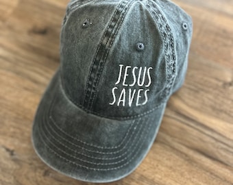 May include: A dark gray denim baseball cap with white embroidered text that reads "JESUS SAVES".
