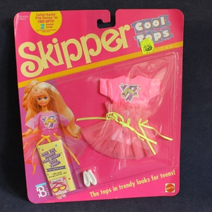 Puede incluir: Un conjunto de moda de muñeca Skipper vintage en su embalaje original. El conjunto incluye una camiseta y falda rosas, zapatos blancos y una muñeca. El embalaje es rosa y amarillo con el texto "Skipper" y "Cool Tops".