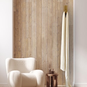 Könnte beinhalten: Ein weißer, flauschiger Sessel mit Holzsockel steht vor einer Holzvertäfelung. Ein kleiner, hölzerner Beistelltisch mit zwei Dekorationsgegenständen steht neben dem Sessel. Ein weißer Überwurf hängt an einem Haken an der Wand.