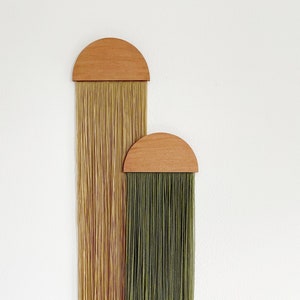 Könnte beinhalten: Zwei Wandbehänge mit halbrunden Holz-Oberteilen. Der obere Behang hat eine hellbraune Franse und der untere Behang hat eine grüne Franse.