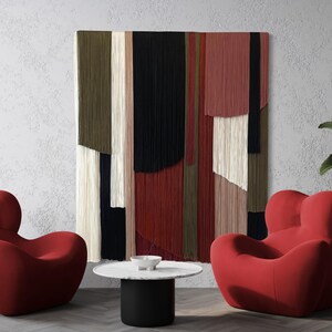 May include: Two red, plush, oversized armchairs with a unique, organic shape, facing each other in a living room setting. A black and white abstract wall hanging with a geometric pattern hangs on the wall behind the chairs. A small, round, black and white coffee table sits between the chairs.