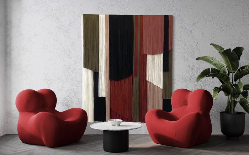 May include: Two red, plush, oversized armchairs with a unique, organic shape, facing each other in a living room setting. A black and white abstract wall hanging with a geometric pattern hangs on the wall behind the chairs. A small, round, black and white coffee table sits between the chairs.