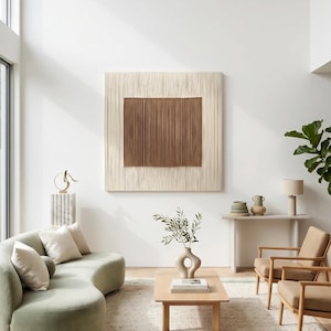 May include: A living room featuring a sage green curved sofa with cream pillows, a light wood coffee table with a sculptural vase, two tan armchairs, a console table with ceramic bowls, and a large square wall art piece with cream and brown fringe.