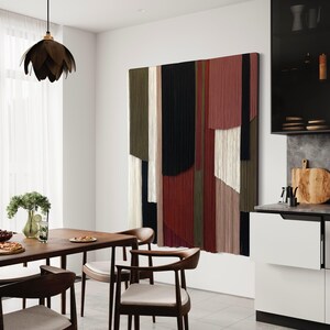 May include: A modern dining room with a wooden table and chairs. The wall features a large abstract wall hanging made of yarn in shades of red, green, black, and white.