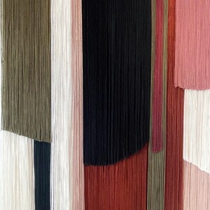 May include: A wall hanging made of yarn in various colors, including green, white, black, red, and pink. The yarn is arranged in vertical stripes, creating a geometric pattern.