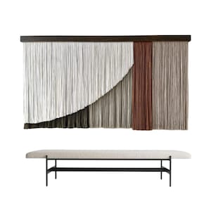 Könnte beinhalten: Ein großer Wandbehang mit dunkler Holzoberseite und einer Kaskade aus strukturierten Fasern in Weiß, Grau, Braun und Beige. Darunter eine lange Bank mit hell gepolsterter Sitzfläche und schwarzen Metallbeinen.