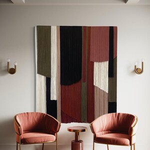 May include: Two pink velvet armchairs with gold metal frames sit facing each other in front of a large abstract wall hanging made of colorful yarn. A small pink side table sits between the chairs.